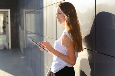 Young woman using digital tablet standing by wall