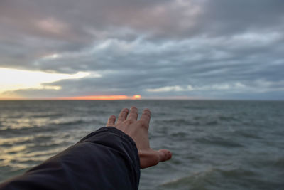 Cropped hand of person against sea during sunset