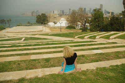 Rear view of woman sitting on field against sky