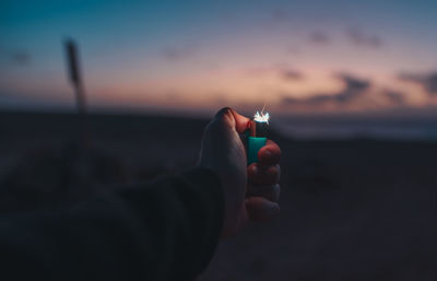 Person holding camera on beach against sky during sunset