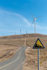 Wind turbines on field by road against sky