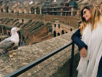 Young female tourist looking at seagull perching on retaining wall at coliseum