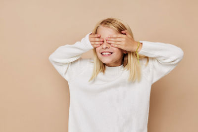 Smiling girl closing eyes against beige background