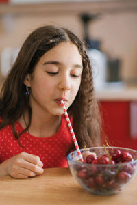 Teenage girl drinks juice from a cherry in a plate through a straw. the concept of an organic drink