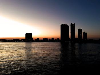 Silhouette buildings by sea against sky during sunset