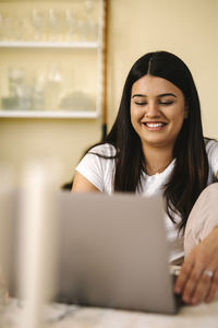 Happy young female freelancer using laptop sitting at table