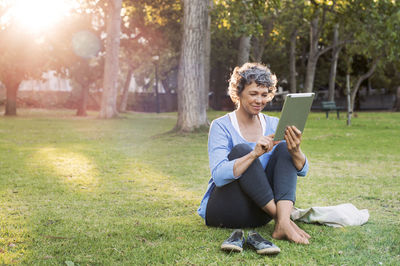 Smiling woman using digital tablet while sitting on grassy field