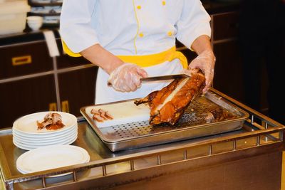 Midsection of chef cutting meat slices in commercial kitchen