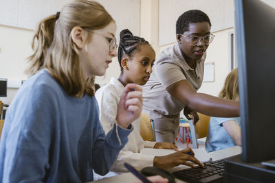 Female teacher pointing at computer while teaching students in classroom at school