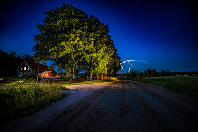 Road amidst trees against clear blue sky at night