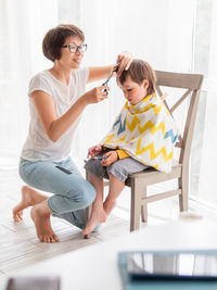 Mother cuts her son's hair by herself. little boy sits, and holds pair of scissors. family life.