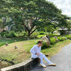 Side view of woman sitting on grassland against trees