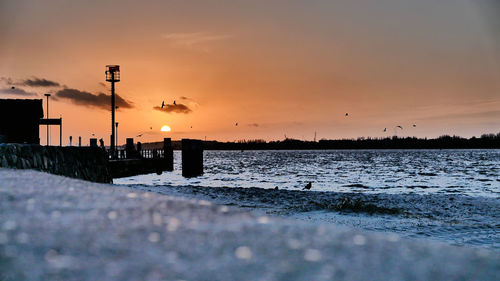 Silhouette street by sea against orange sky