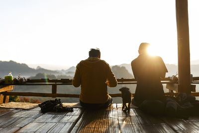 Rear view of male friends sitting with puppy at balcony against clear sky