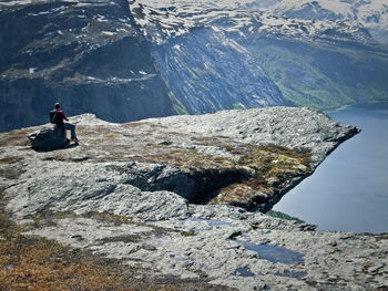 Man sitting on rock at cliff over lake