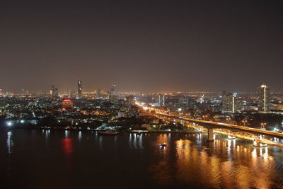 Illuminated city by river against sky at night