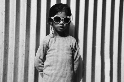 Portrait of girl wearing sunglasses standing against wall