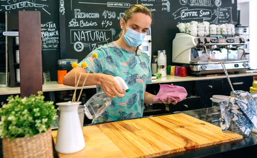 Woman wearing mask spraying sanitizer on counter in cafe