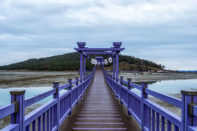 Rear view of woman walking on footbridge against sky