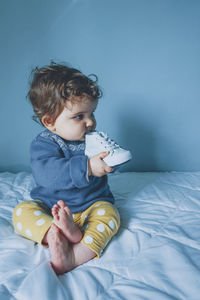 Baby girl looking away while sitting on bed at home