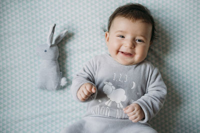 Portrait of smiling baby girl lying on bed beside toy bunny