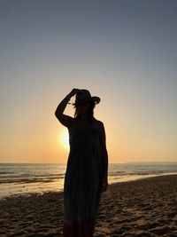 Woman standing on beach against sky during sunset