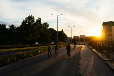 People riding motorcycle on road against sky during sunset