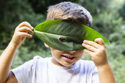 Portrait of cute smiling boy looking through hole in leaf