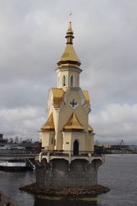 View of building by river against cloudy sky