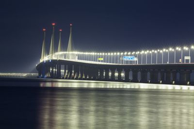 Illuminated bridge over sea against sky at night