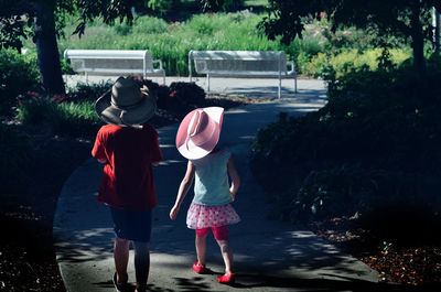 Rear view of siblings wearing hats while walking on footpath at park