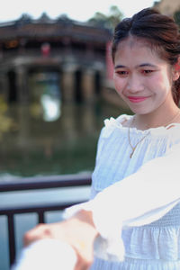 Smiling woman holding hand while looking down against railing