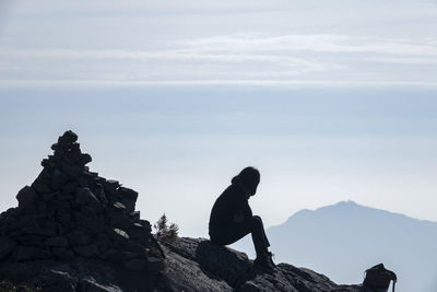 Man sitting on rock against sky