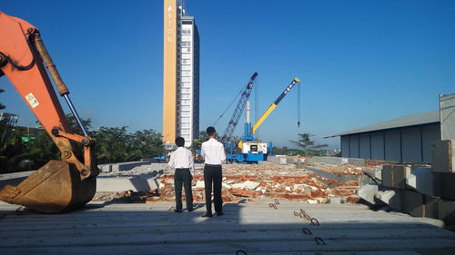 Rear view of men standing on construction site against clear blue sky