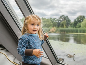 Girl looking away while standing by window in boat
