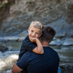 Like father like son. middle aged father embracing cute little son on the bank of river, family