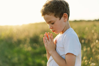 Boy closed her eyes and praying in a field at sunset