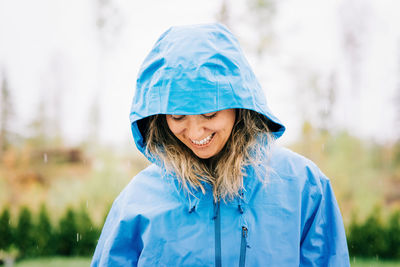 Woman stood in the rain with a raincoat on smiling outside