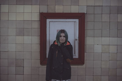 Young woman looking away while standing against wall