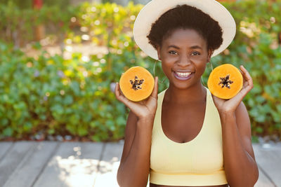 Portrait of a charming african girl in a straw hat with a papaya in her hands.