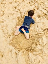 High angle view of carefree boy lying on sand at beach