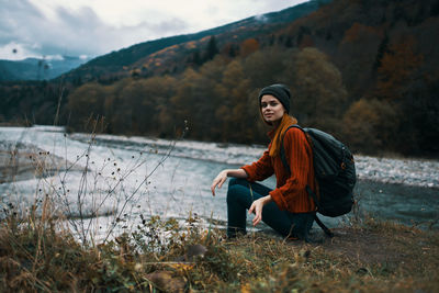 Side view of young woman sitting on shore against mountains