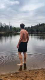 Rear view of shirtless man standing in lake against sky