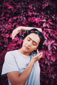 Beautiful young woman with pink flower standing against plants