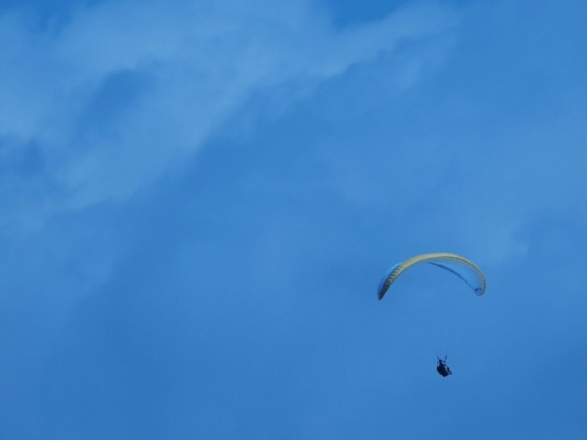 low angle view, blue, mid-air, flying, parachute, adventure, sky, extreme sports, paragliding, leisure activity, exhilaration, sport, fun, nature, day, beauty in nature, unrecognizable person, outdoors, one person, tranquility