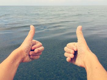 Cropped image of person gesturing ok sign against sea