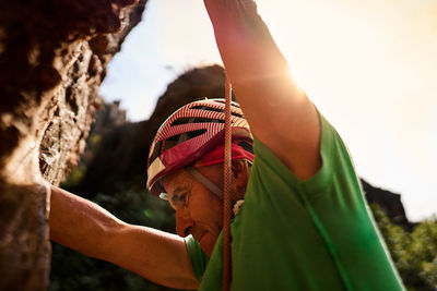 From below side view unrecognizable active fit senior man climbing on rocky cliff