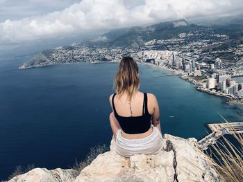Rear view of woman sitting on cliff against cityscape