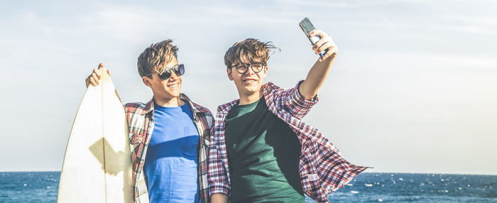 Two young boys at the beach near ocean taking picture with cell phone students on vacation with surf