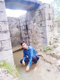 Full length of man sitting on rock against wall